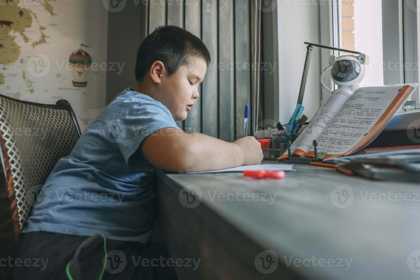 asian boy write in notebook, homework beside open textbook on desk, study tool, education, homeschooling, parenting resources photo