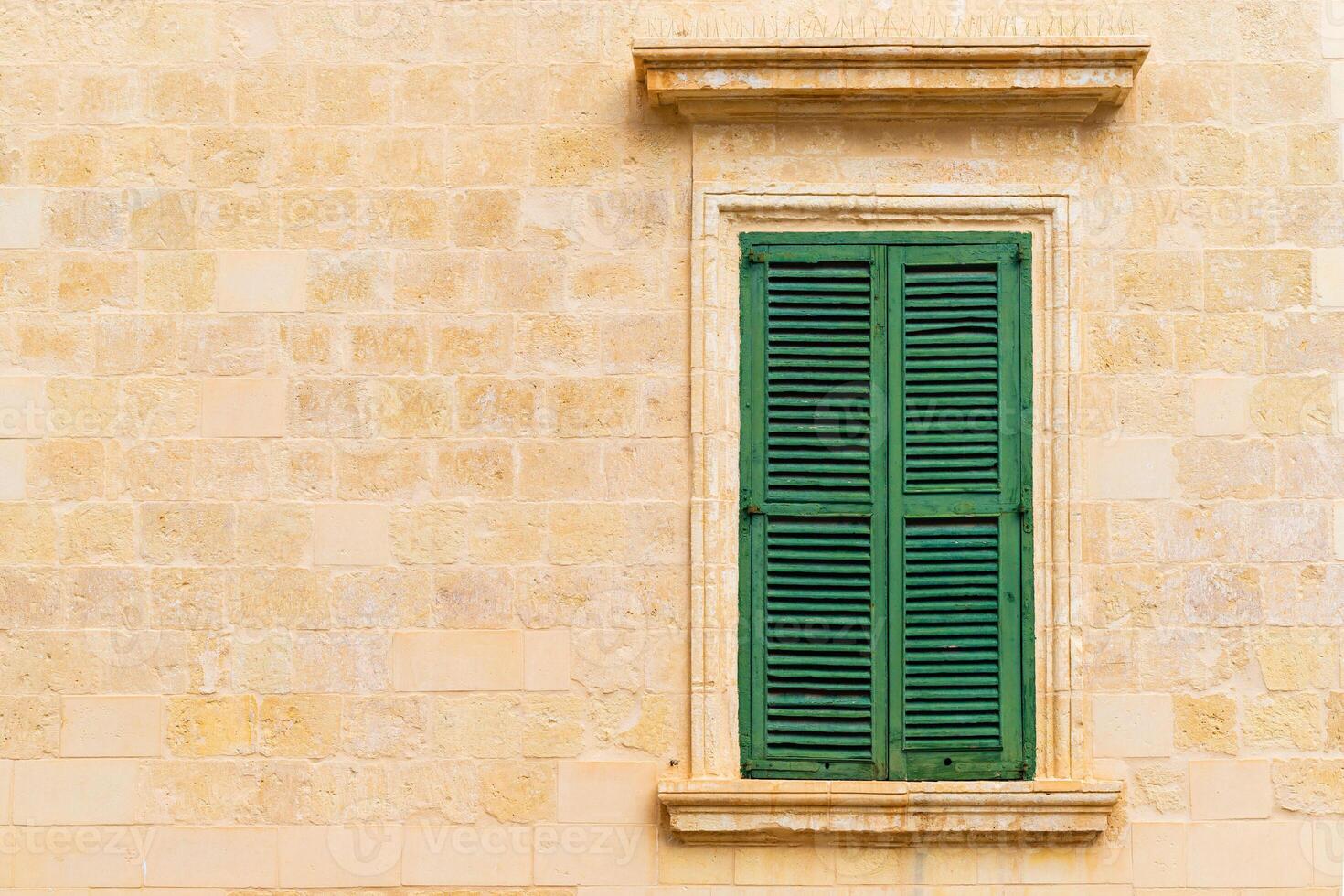 Stone brick wall with a closed green wooden window with shutters photo