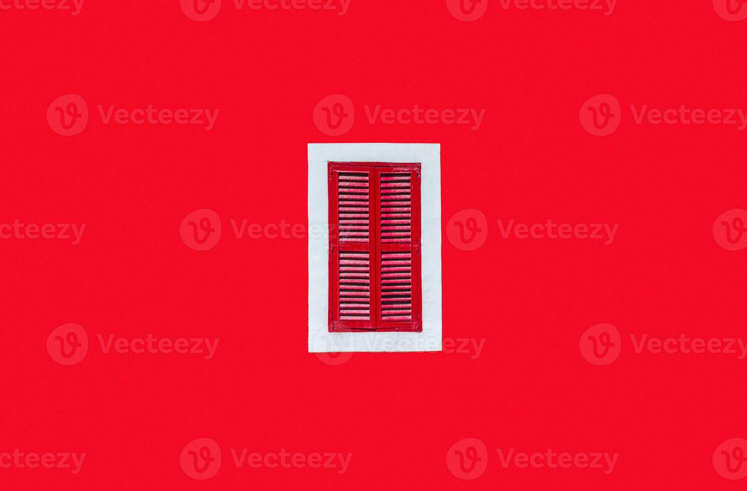 Plain red wall with a red window in a white frame in the middle of the shot photo