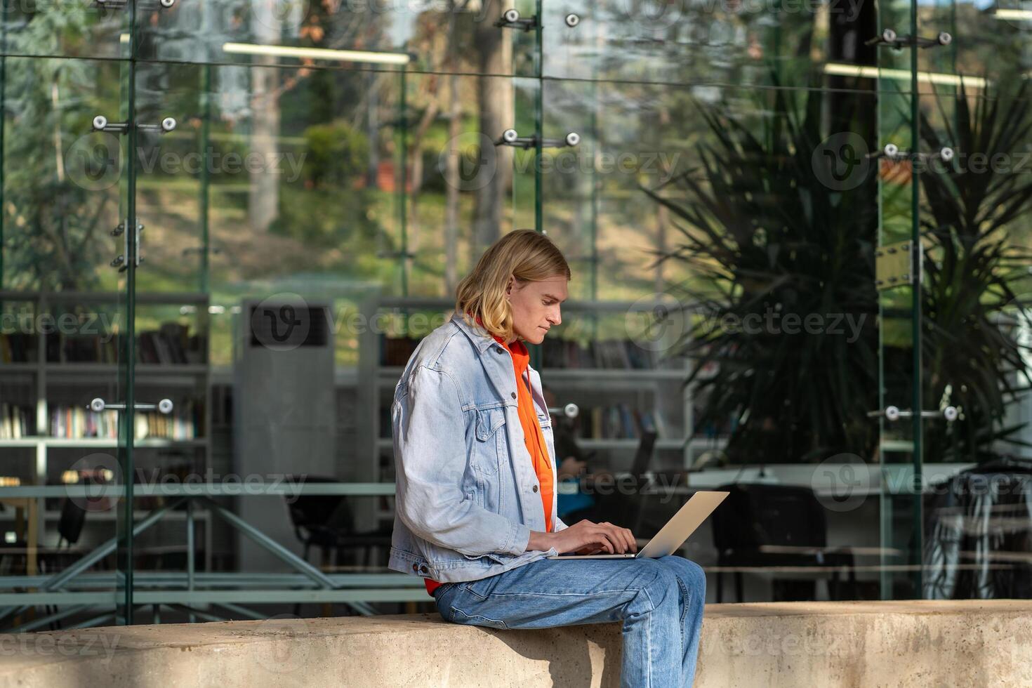 Focused man with laptop sits near modern building works as programmer in IT company outdoor. photo