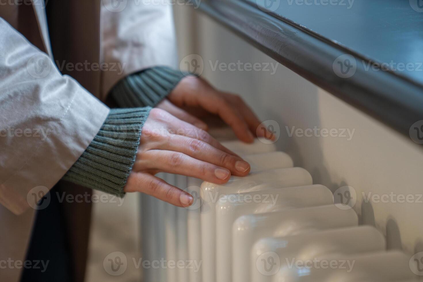Woman warming hands near old vintage radiator at home, checking heating system working capacity photo