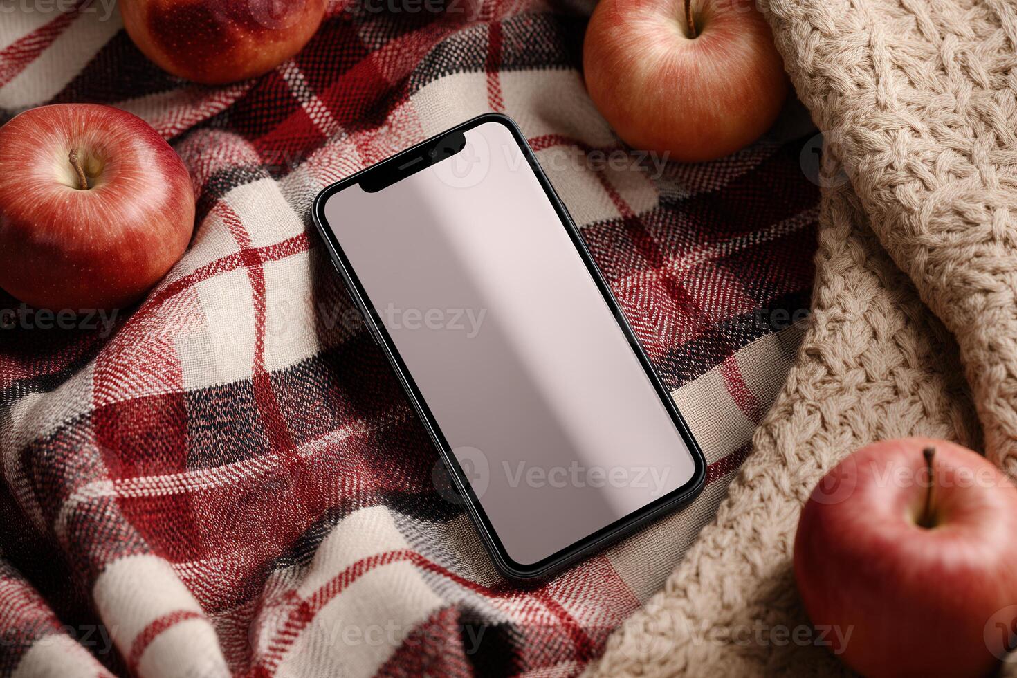 A smartphone on a red plaid blanket with apples and knitted fabric in warm, soft lighting. Great for autumn-themed promotions, lifestyle scenes, and mobile app mockups. photo