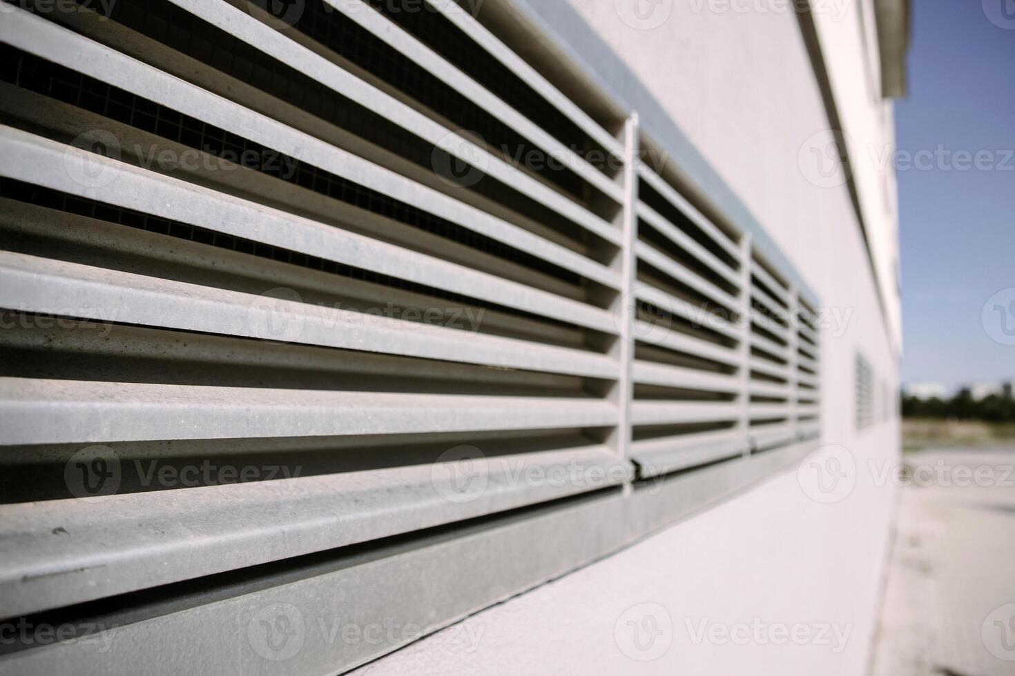 A metal ventilation grille mounted on the wall of a modern industrial building. Great for illustrating concepts of airflow, HVAC systems, construction, and urban infrastructure. photo