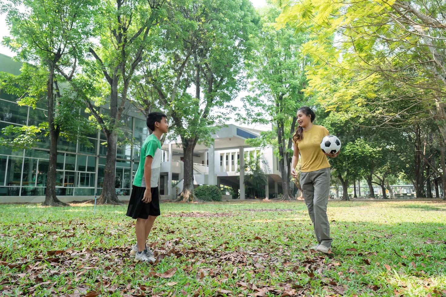 Playful Interaction and Soccer Fun. A young boy and woman enjoying a game of soccer in a park. photo