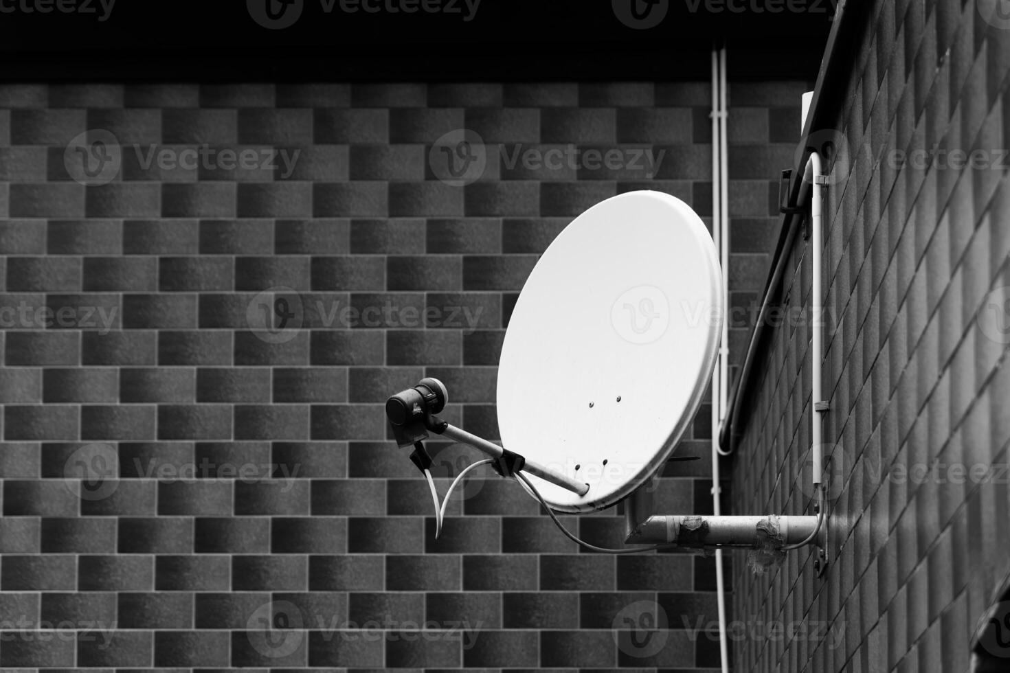 Brushed metal satellite dish rests against a textured brick wall in shadowy tones at dawn, capturing the quiet of early morning photo