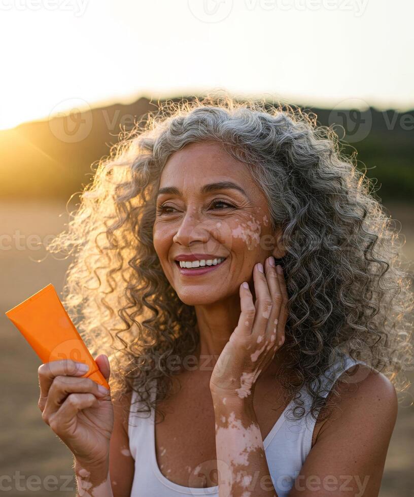 Mature woman with vitiligo smiling and holding tube of sunscreen cream. Embracing natural beauty, self-care, and healthy skin routine. For projects related to diversity, self-love or skin conditions. photo