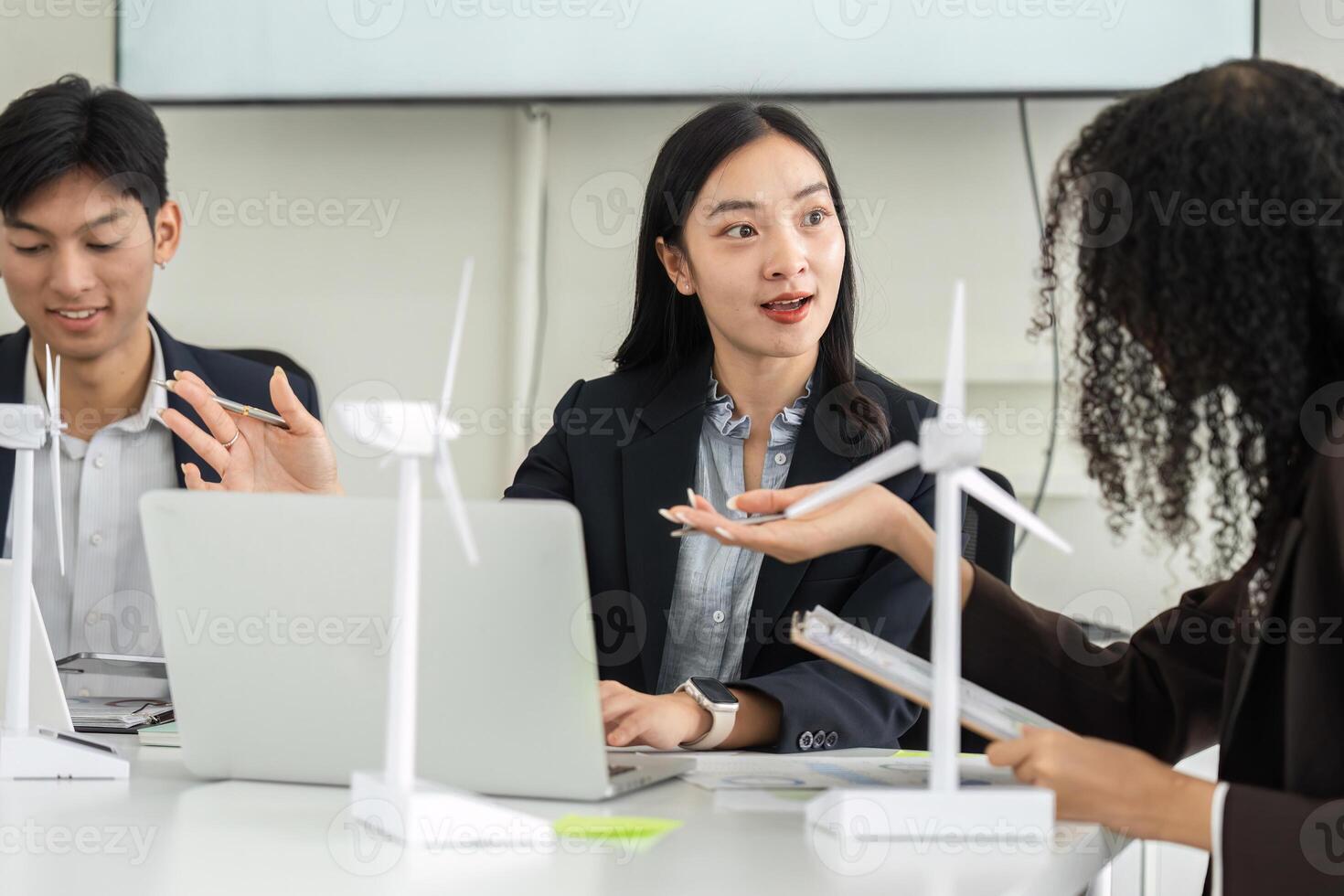Discussion and Innovation in Sustainability. A diverse team collaborates on sustainable energy solutions using wind turbine models in an office setting. photo