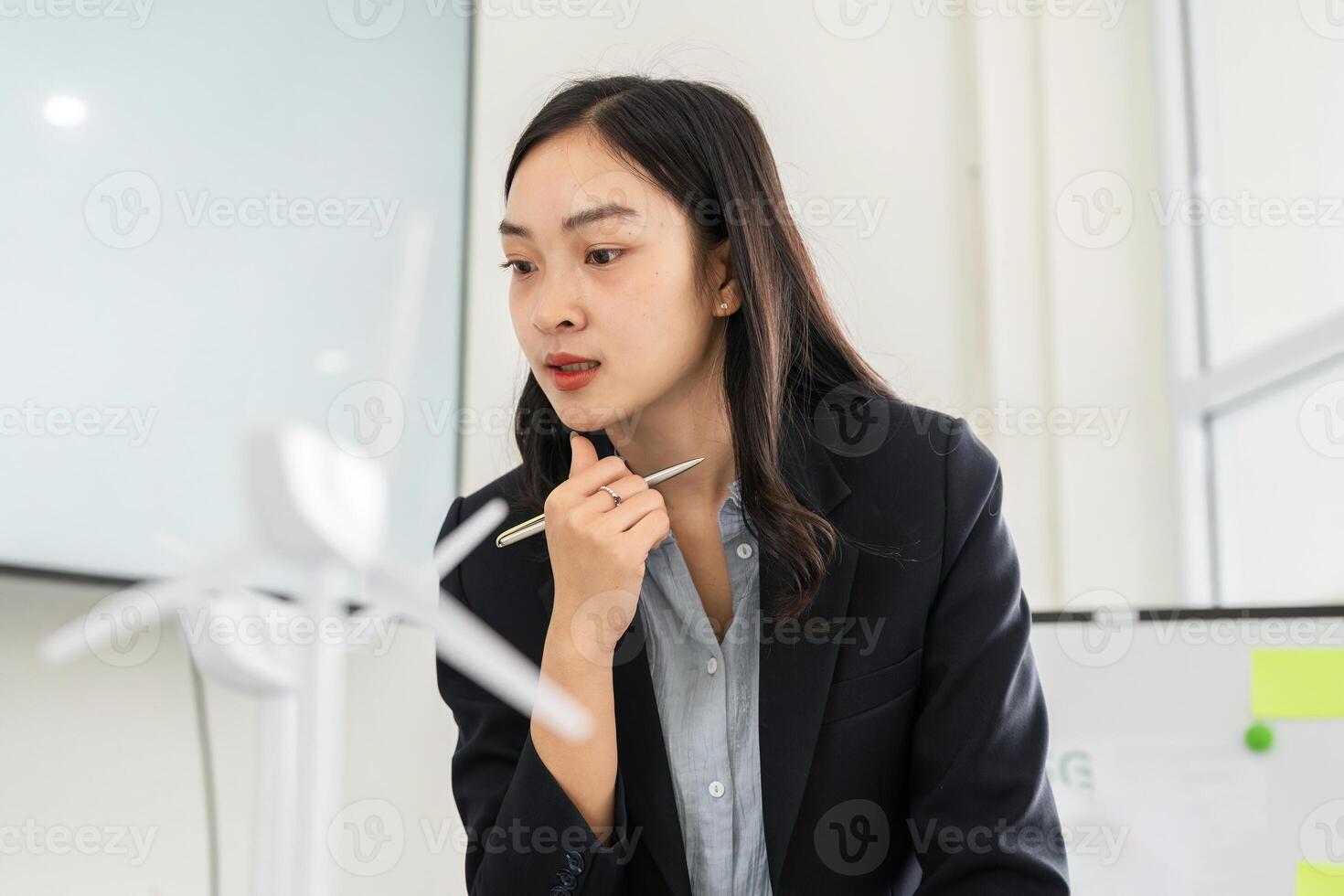 Strategic Planning in Sustainability. A businesswoman contemplating sustainable energy solutions with a wind turbine model. photo