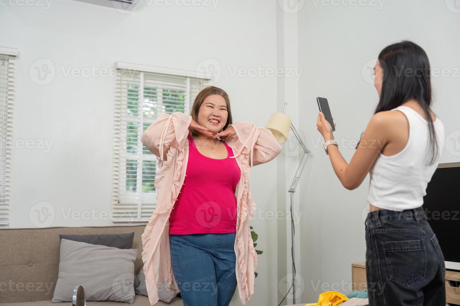 Joyful Moments and Outfit Showcase. A woman smiles brightly in a pink top while her friend snaps a photo, capturing the moment. photo