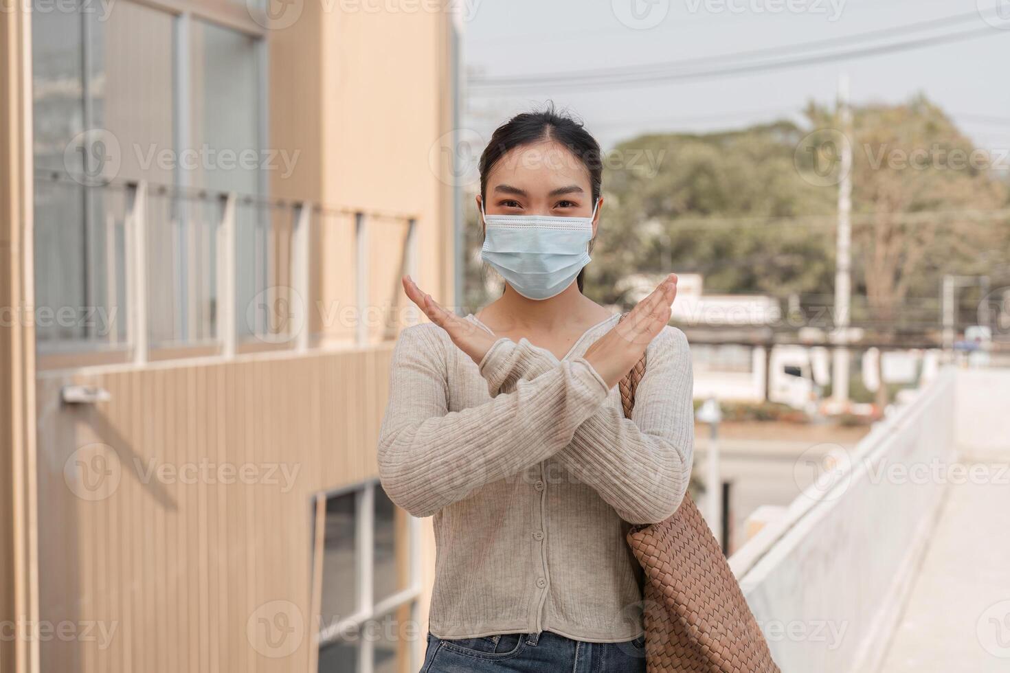Diverse woman in a mask making a stop gesture outdoors in an urban environment. photo