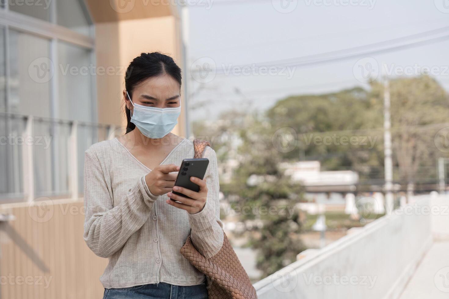 Young woman wearing a mask and texting on her smartphone outdoors in a public area. photo