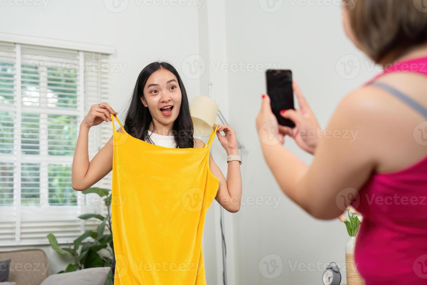 Fashion and Friendship. A young woman excitedly models a bright yellow dress while her friend captures the moment on her phone. photo