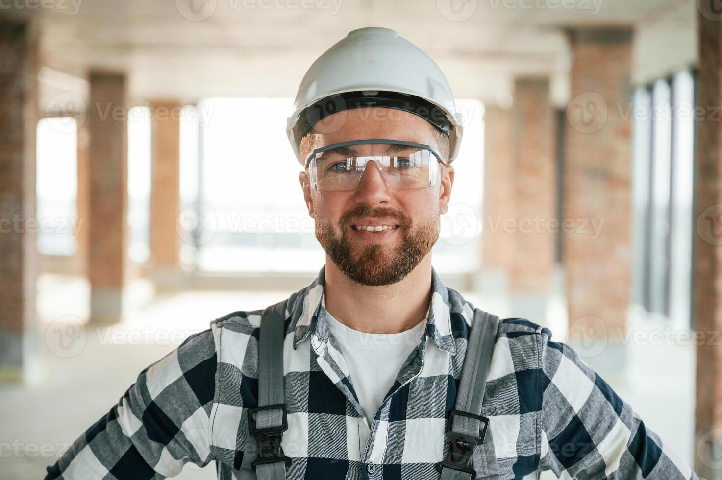 Positive, smiling construction worker in uniform in empty unfinished room photo