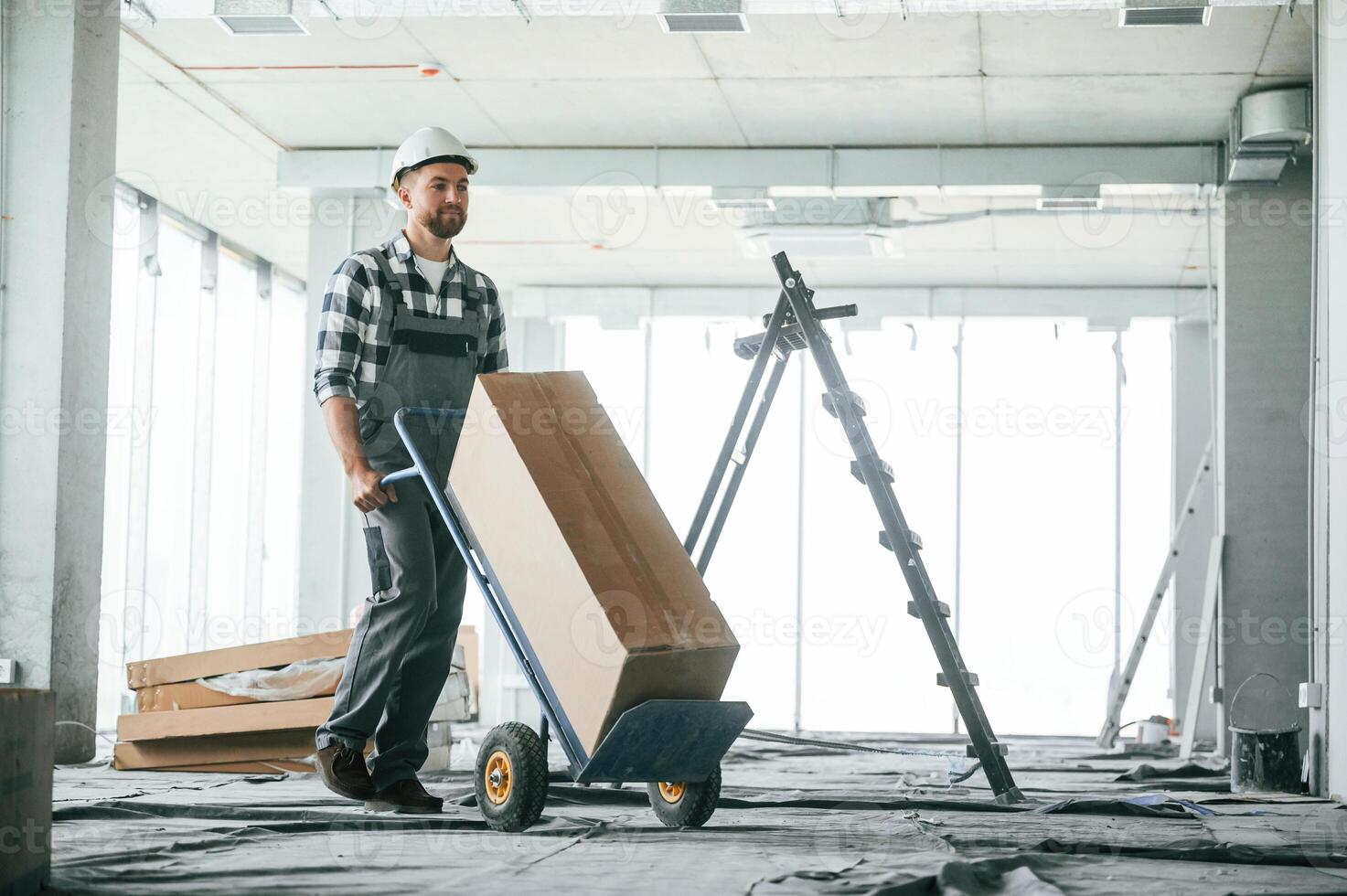 Transporting, long paper box. Construction worker in uniform in empty unfinished room photo