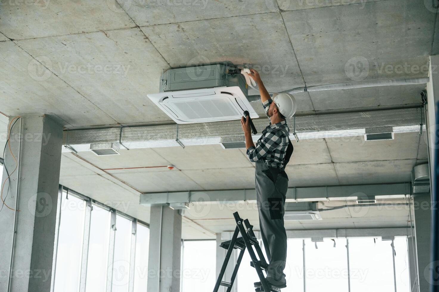 Setting the, ventilation, system. Repairman in uniform is in the unfinished building photo