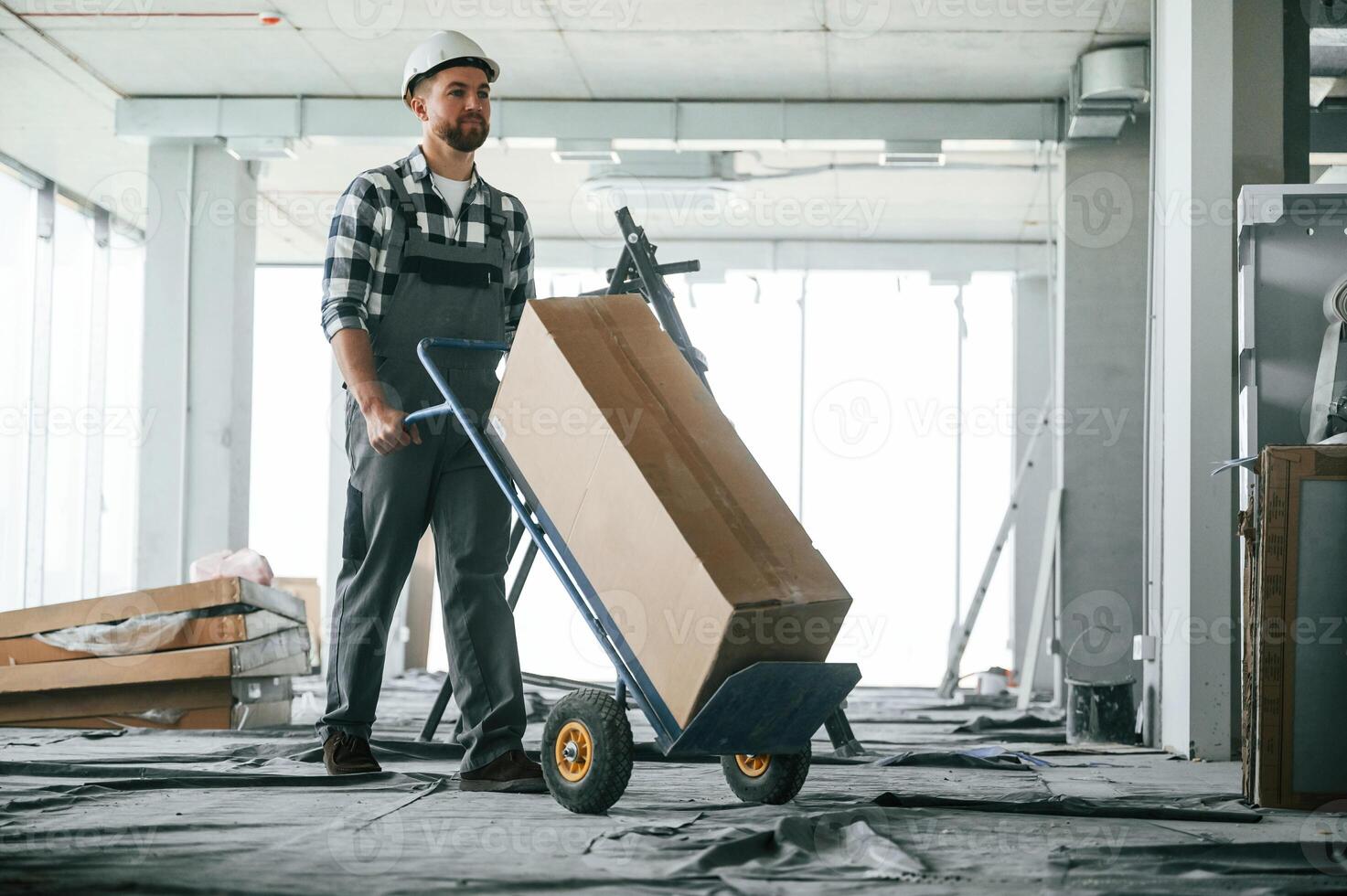 Transporting long paper box. Construction, worker in uniform in empty unfinished room photo