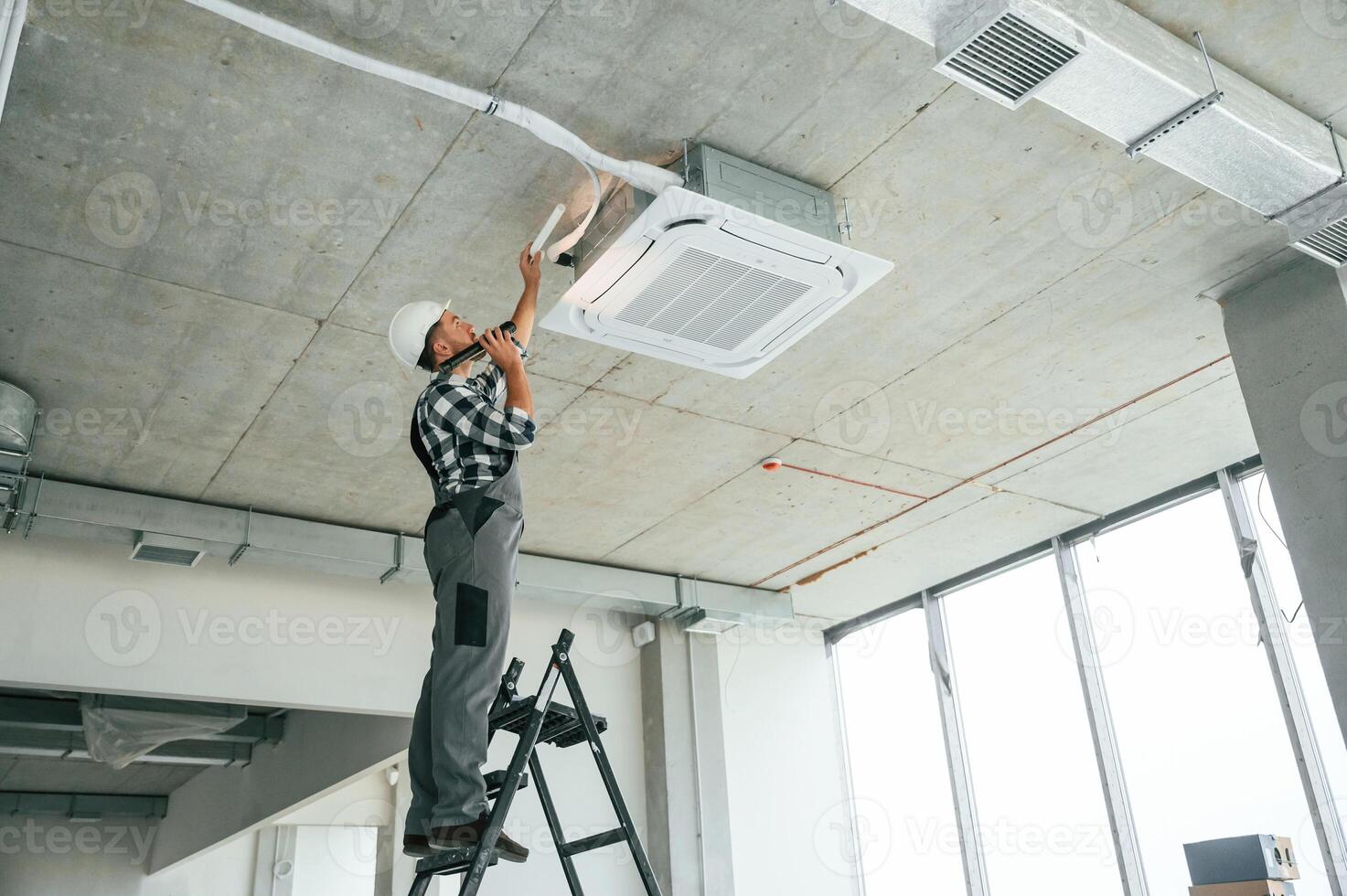 Fixing ,,ventilation ,system. Repairman in uniform is in the unfinished building photo