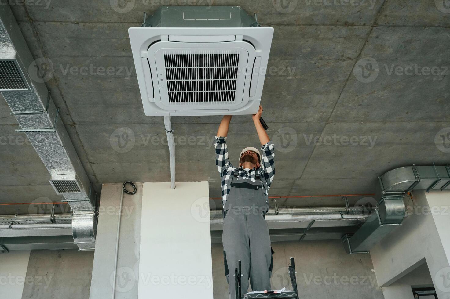 Setting up the ventilation system on the ceiling. Repairman in uniform is in the unfinished building photo