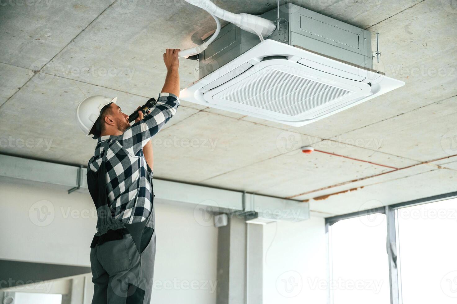 Fixing ventilation system,. Repairman in uniform is in the unfinished building photo