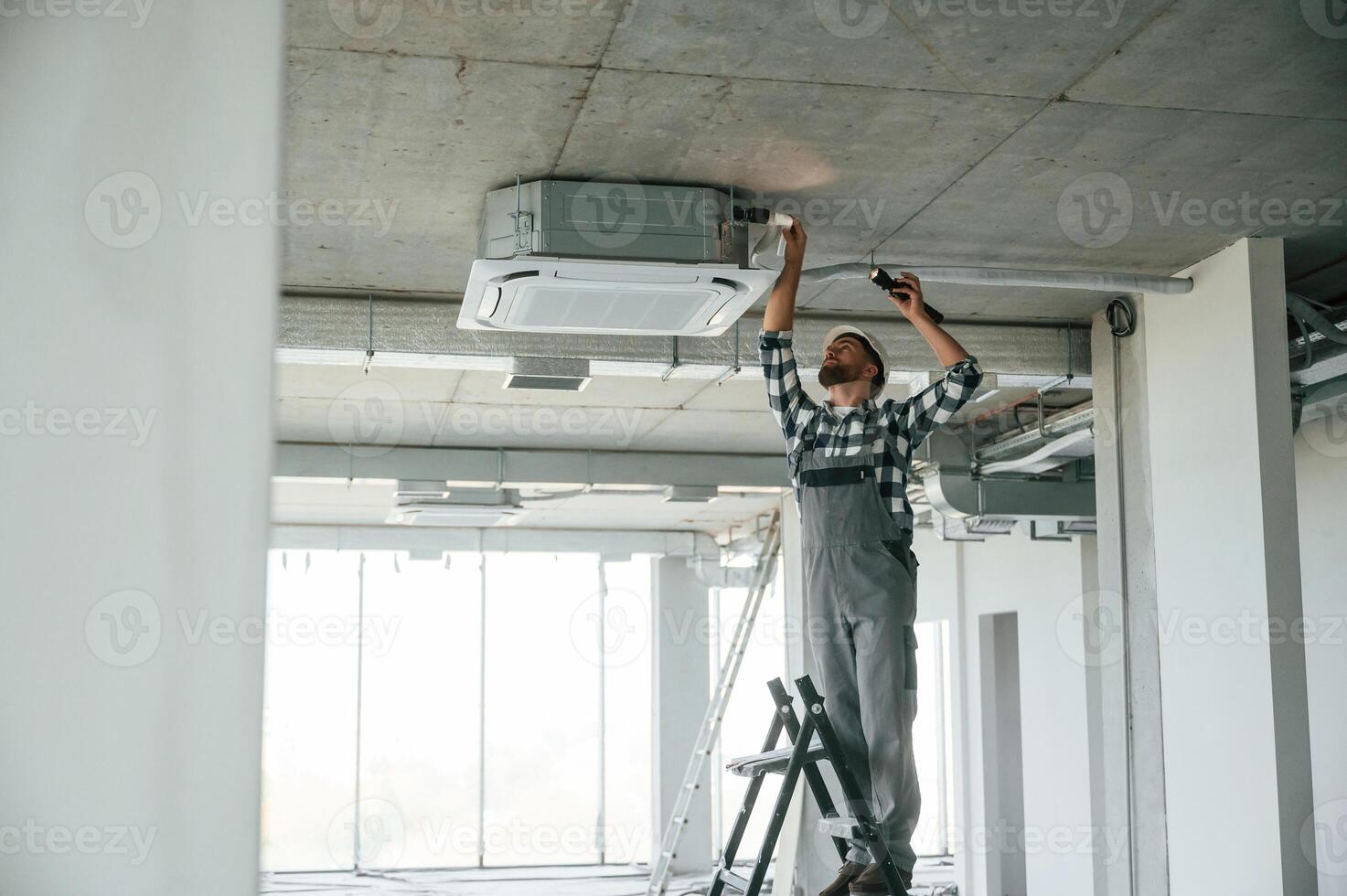 Setting the ventilation, system,. Repairman in uniform is in the unfinished building photo