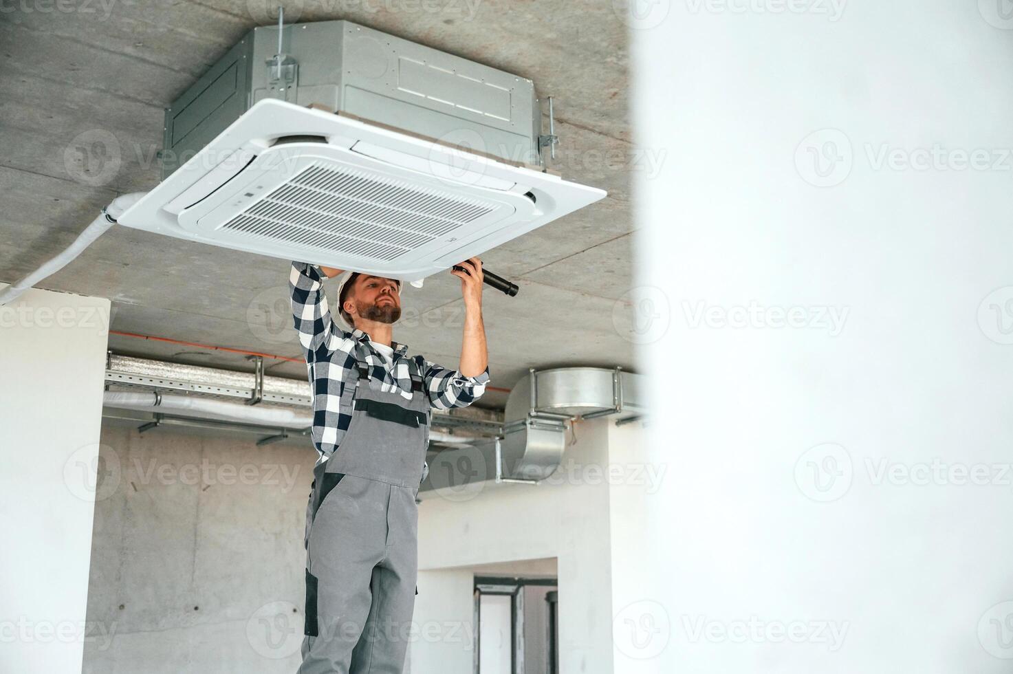 Setting,the ventilation system., Repairman in uniform is in the unfinished building photo