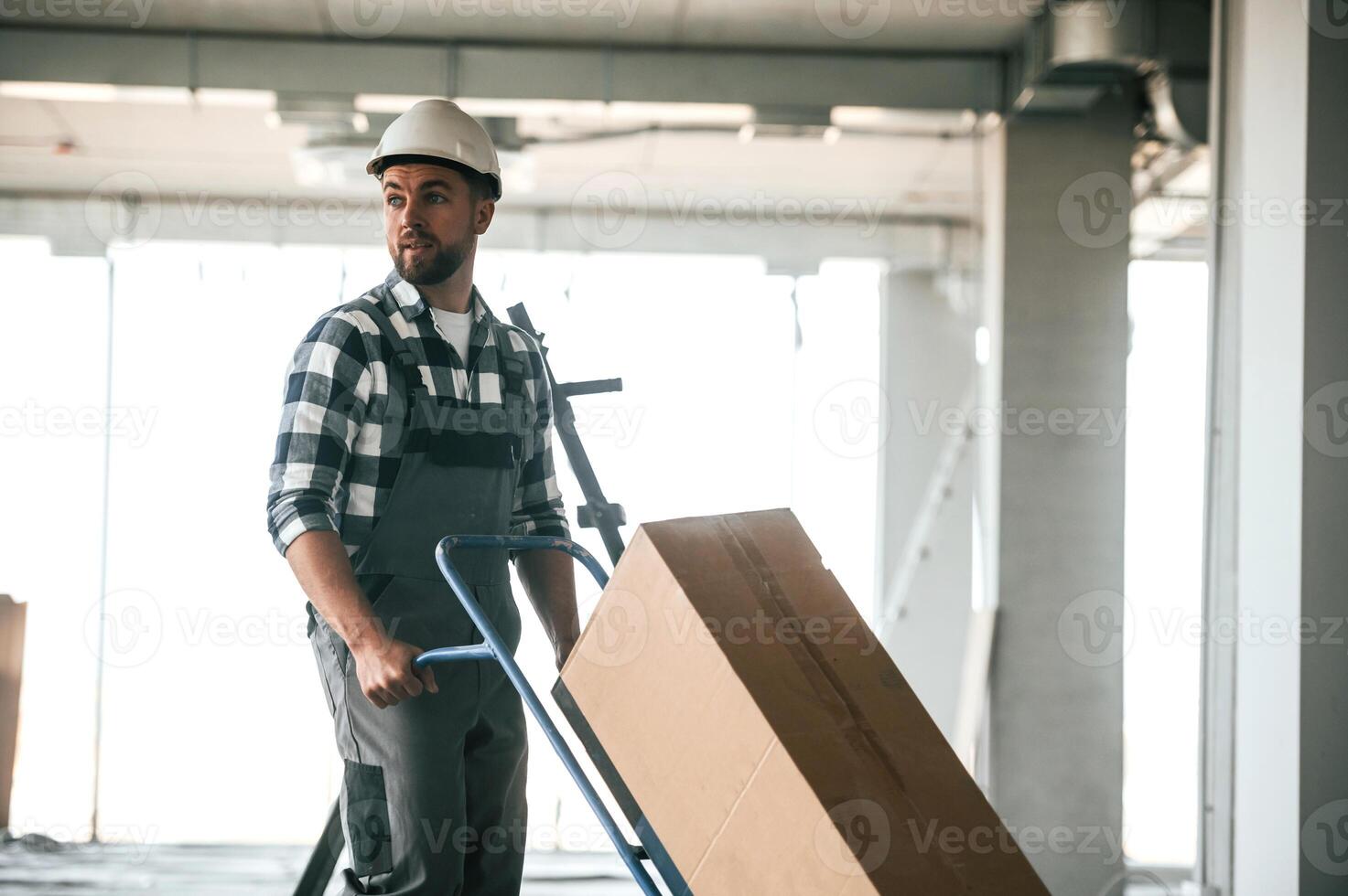 Walking and, transporting the paper box. Repairman in uniform is in the unfinished building photo