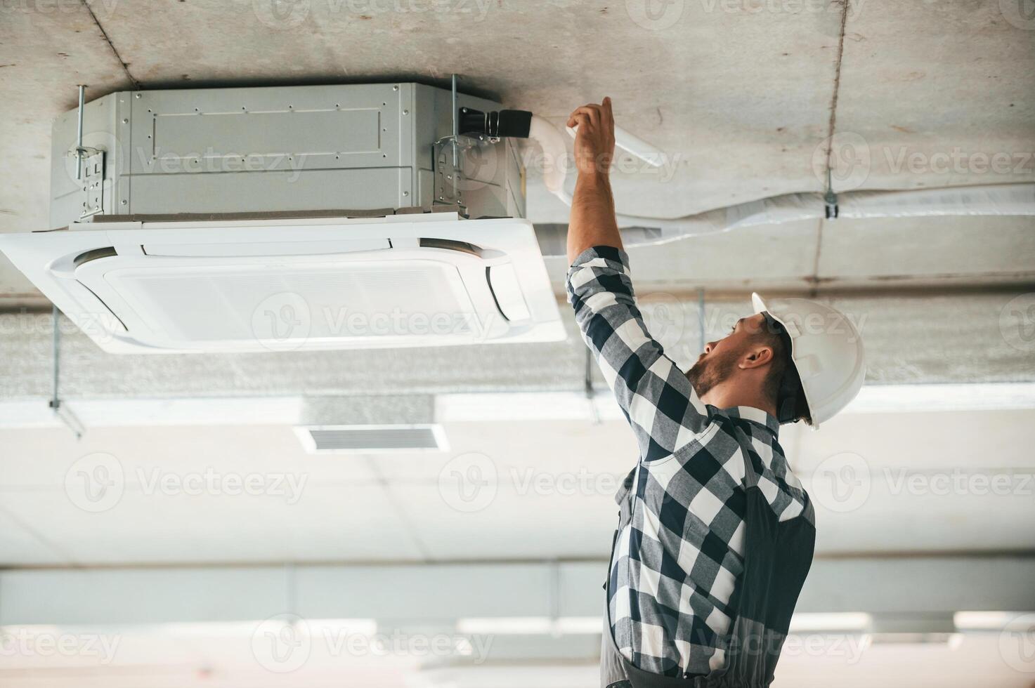 Ventilation ,system high up on the ceiling, fixing. Repairman in uniform is in the unfinished building photo