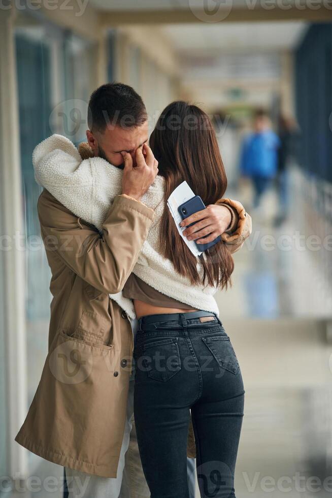 Man is crying, embracing, farewell.. Couple, are in the airport hall together photo