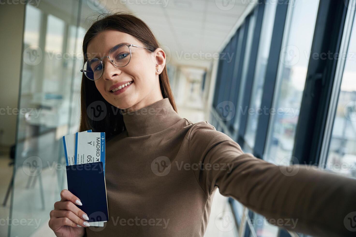Smiling, holding tickets. Young woman traveler in the airport entrance hall photo