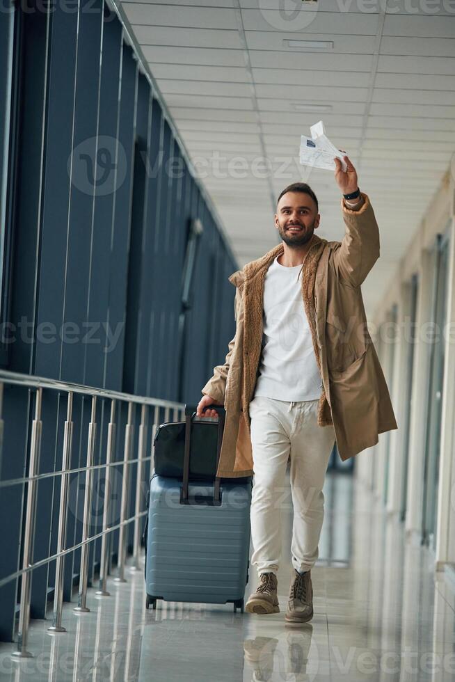 Running, late for flight, with tickets ,in hand. Young handsome man in the airport photo