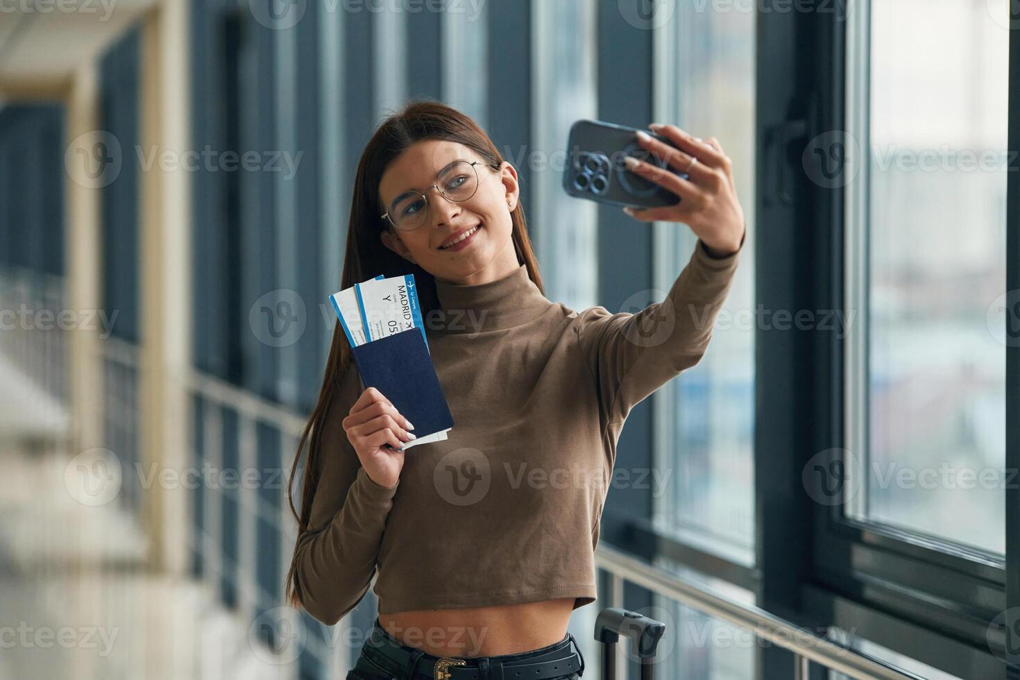 Making selfie ,with phone, smiling. Young woman traveler in the airport entrance hall photo