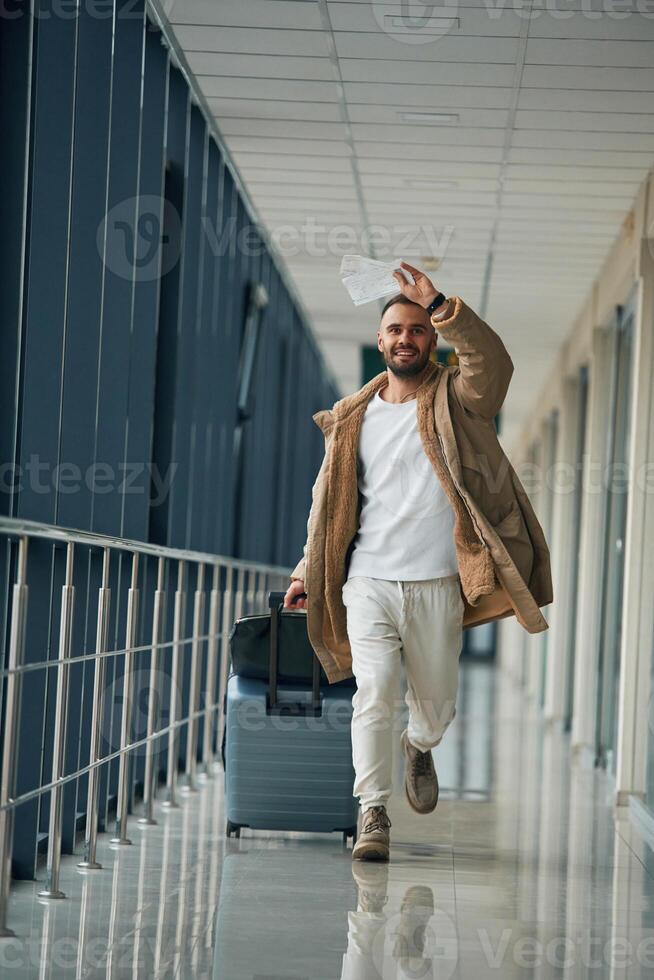 Running,, late for flight, with tickets in hand. Young handsome man in the airport photo