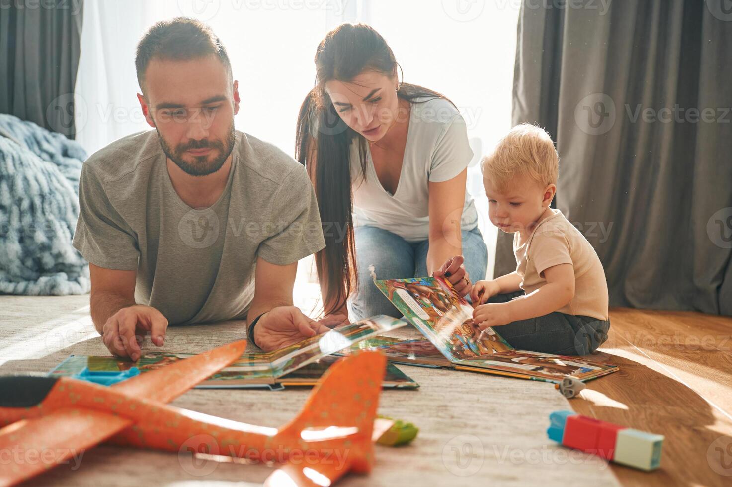 Two parents,, are playing with little son on the floor. Bunch of toys photo