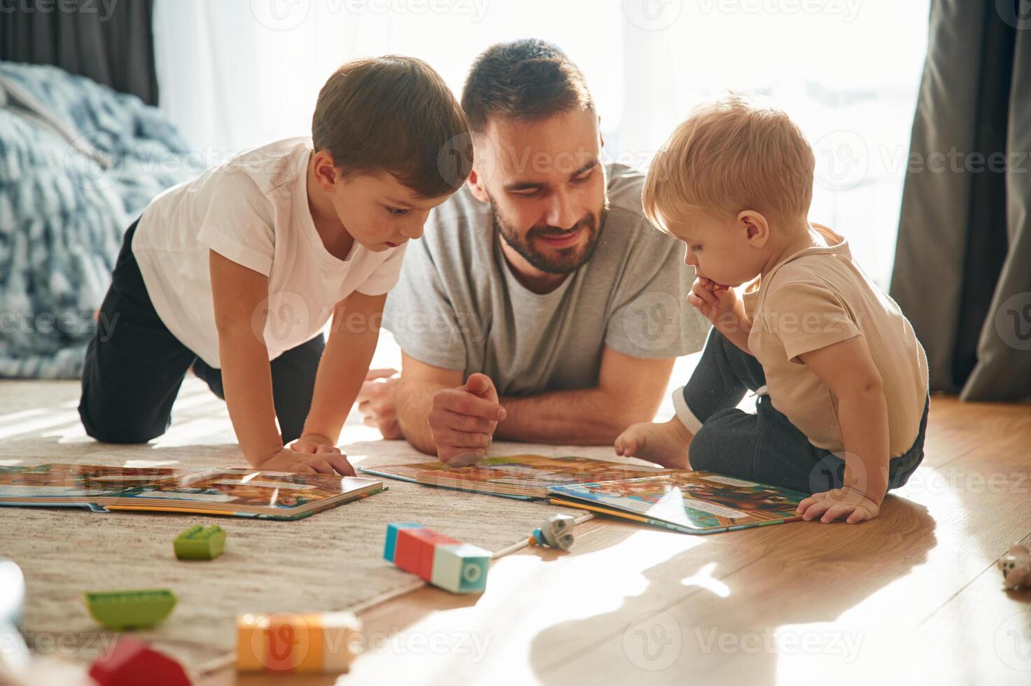 Lying down, ,,board game. Father is playing with two little boys on the floor with toys photo