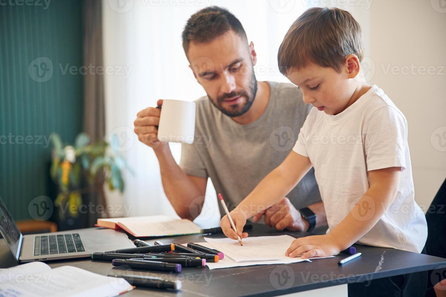 Doing homework.. Father ,and son are at home by the table photo