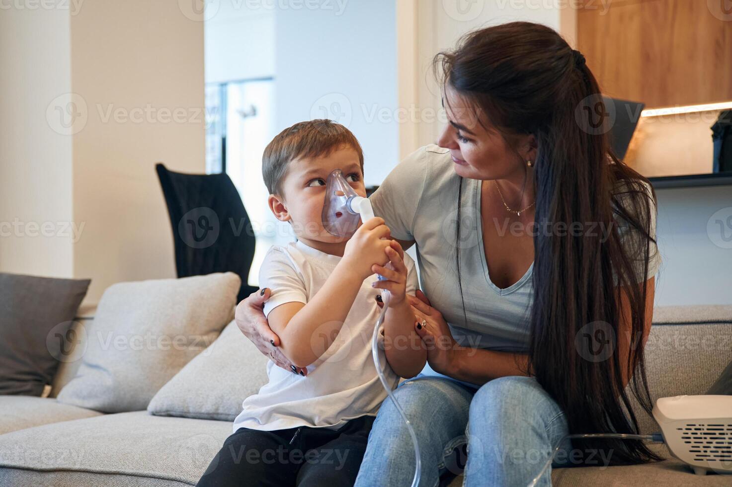 Inhalation for reducing the coughing. Mother with her little son is at home in domestic room photo