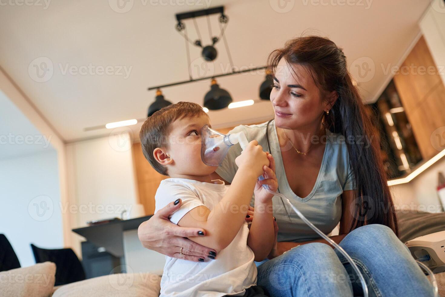 Inhalation with, nebulizer to reduce coughing. Mother with her little son is at home in domestic room photo