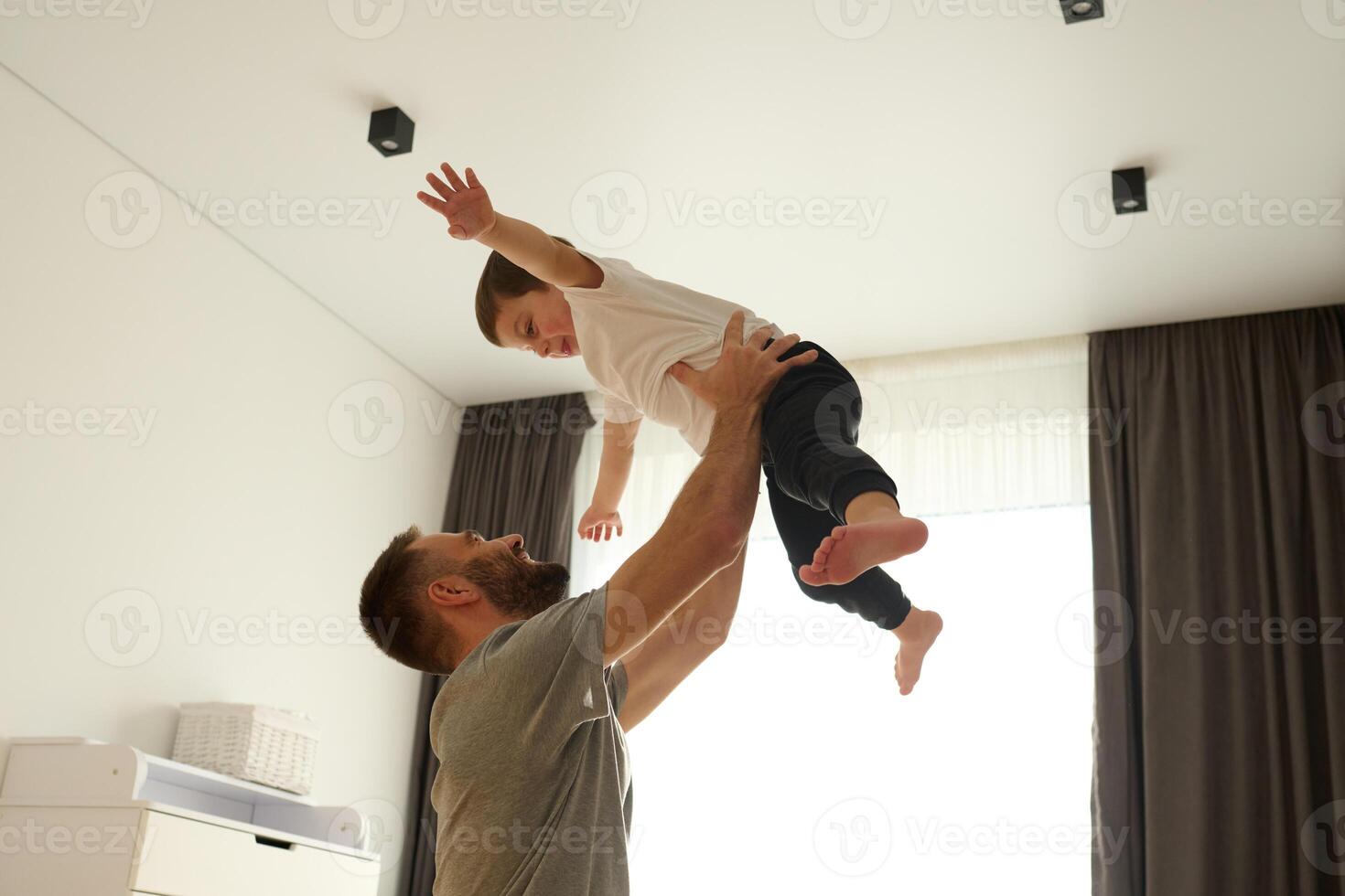 Boy, is imagining that he, is flying. Father holding him. Man is playing with his little son in the domestic room photo