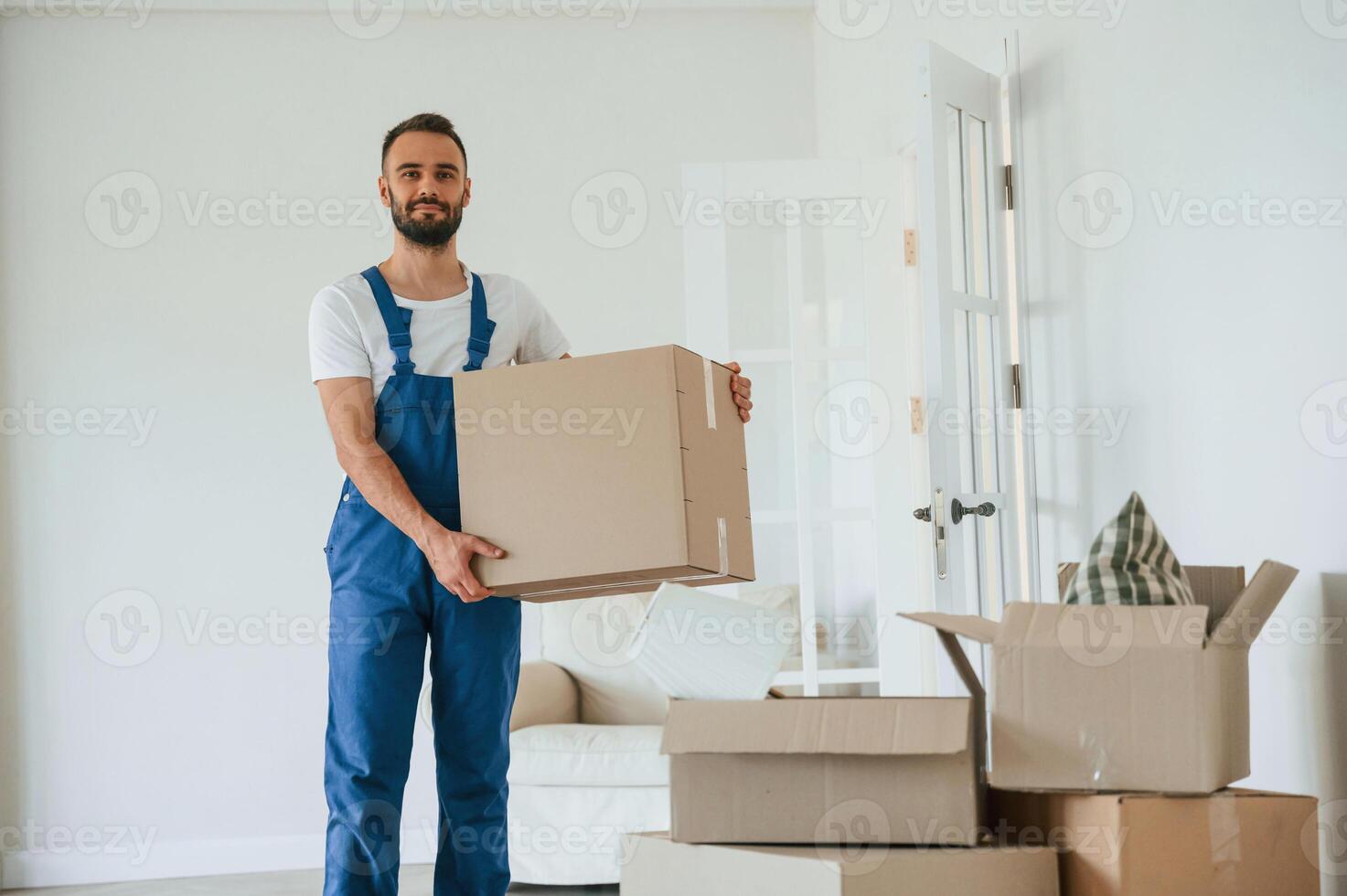 Looking at the camera, holding box. Moving service employee in a room photo