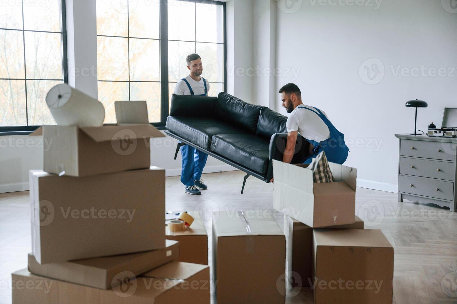 Sofa in hands. Two moving service employees in a ,,room photo