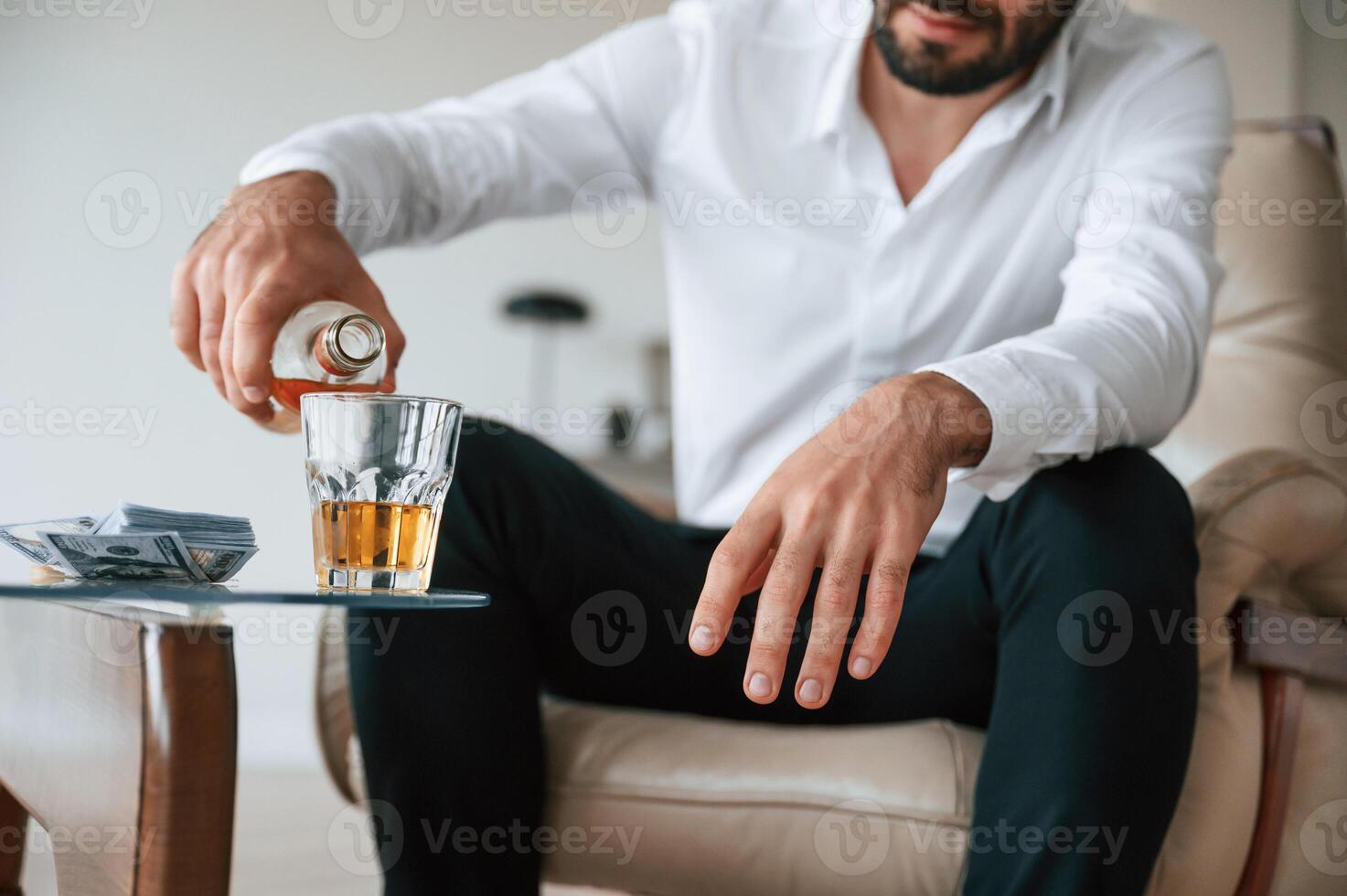 Pouring, the whiskey into the glass. Upset young man drinker alcoholic is indoors photo