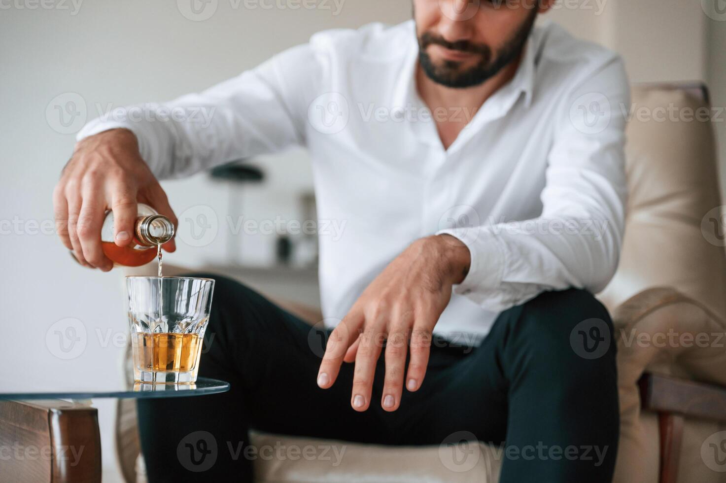 Pouring the, whiskey into the glass. Upset young man drinker alcoholic is indoors photo