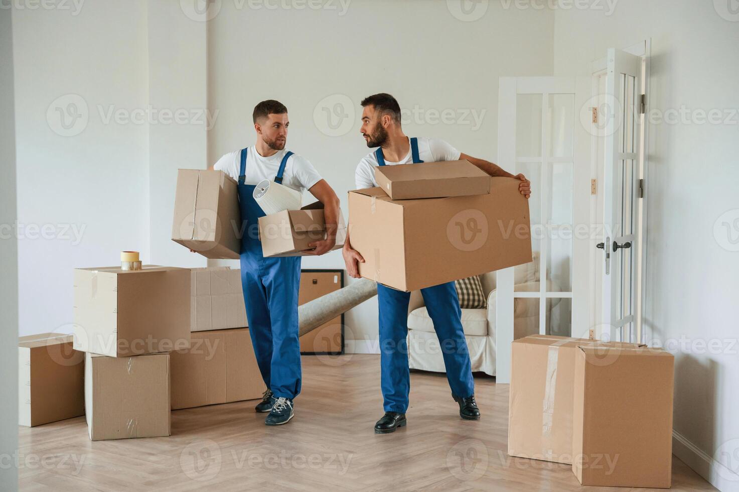 Boxes in hands. Two moving service, employees in a room photo