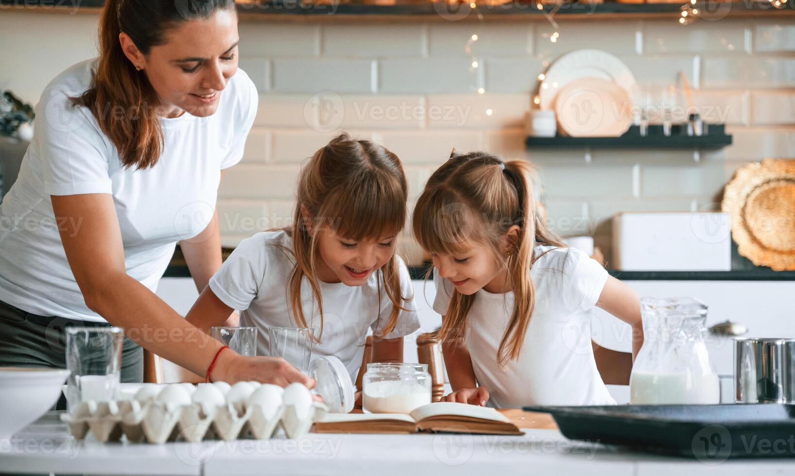 Using quality products. Mother with her little two daughters is preparing food on the kitchen with garlands together photo