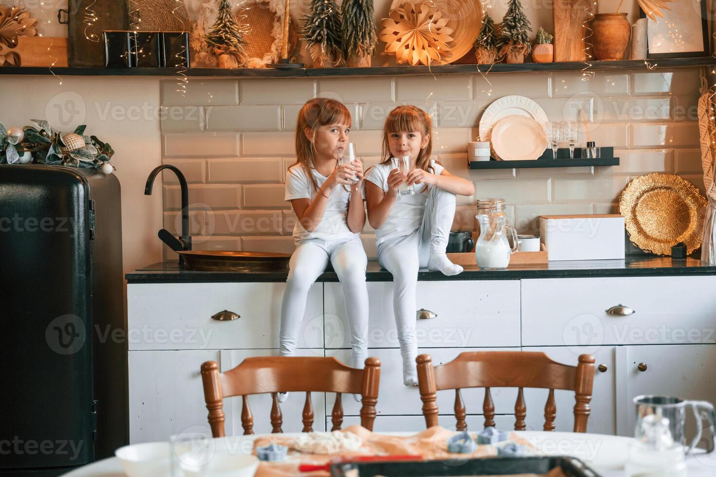 Having fun. Happy, two, little girls are drinking milk while sitting on the table on the kitchen photo
