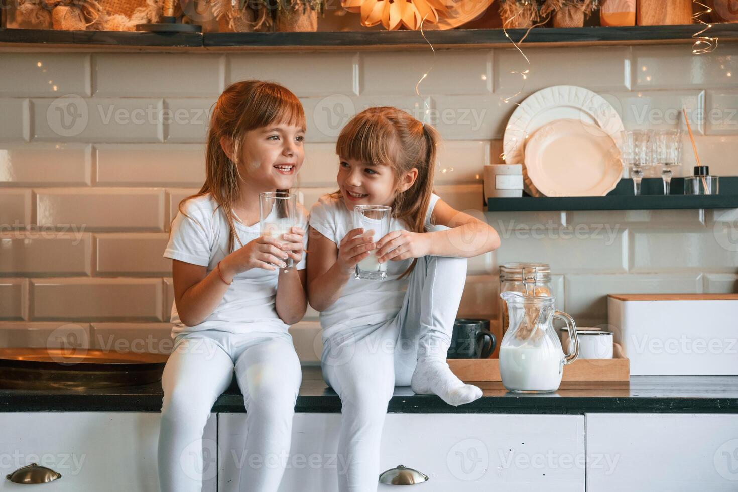 Having, fun.. Happy two little girls are drinking milk while sitting on the table on the kitchen photo