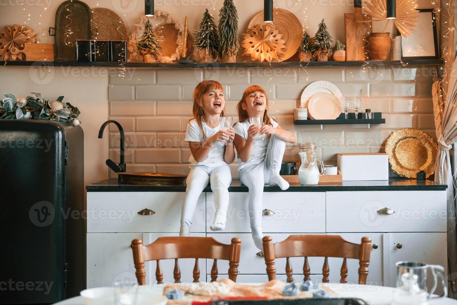Having fun.. Happy two little girls are drinking milk while sitting on the table on the kitchen photo