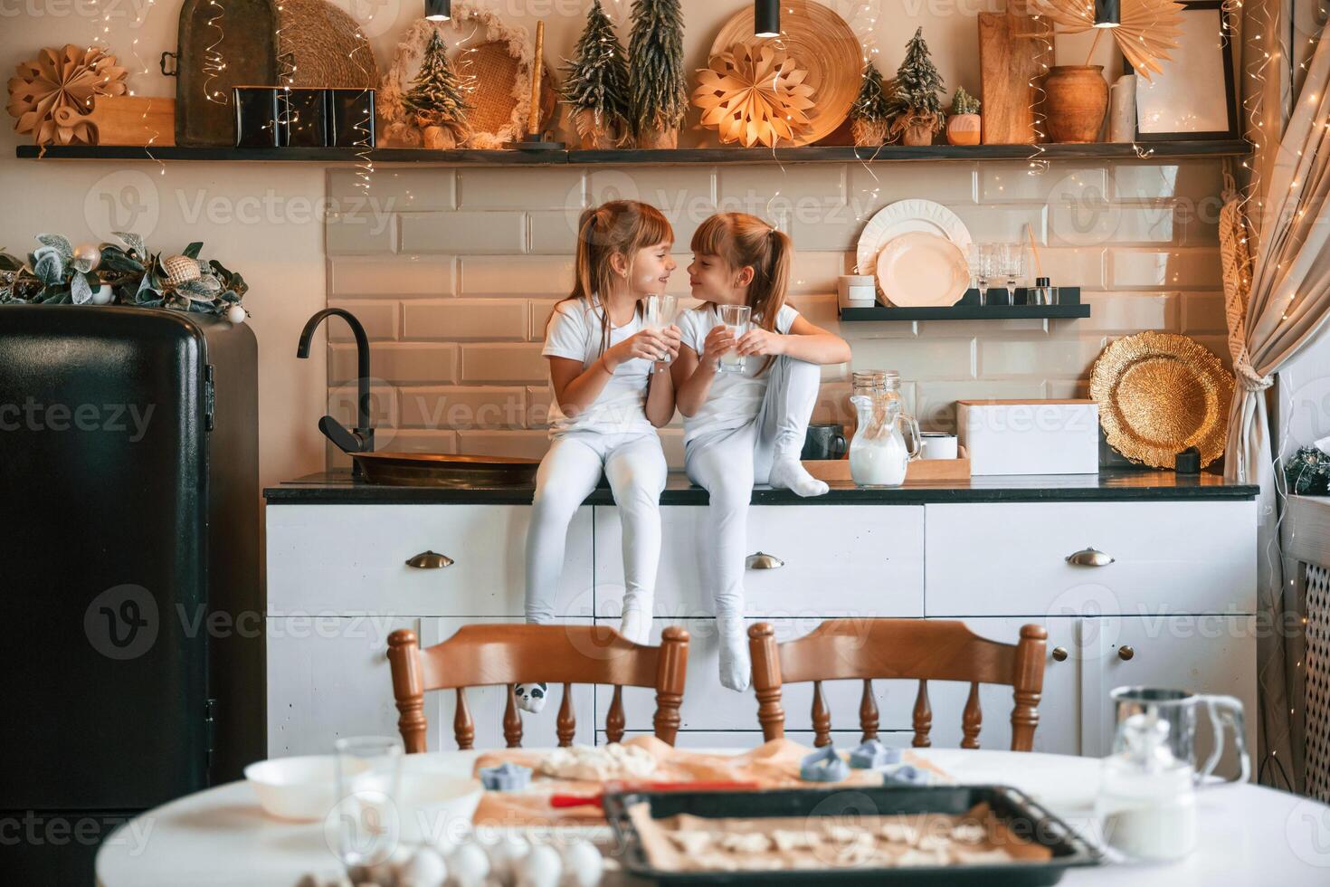 Having, fun. Happy two little girls are drinking milk while sitting on the table on the kitchen photo
