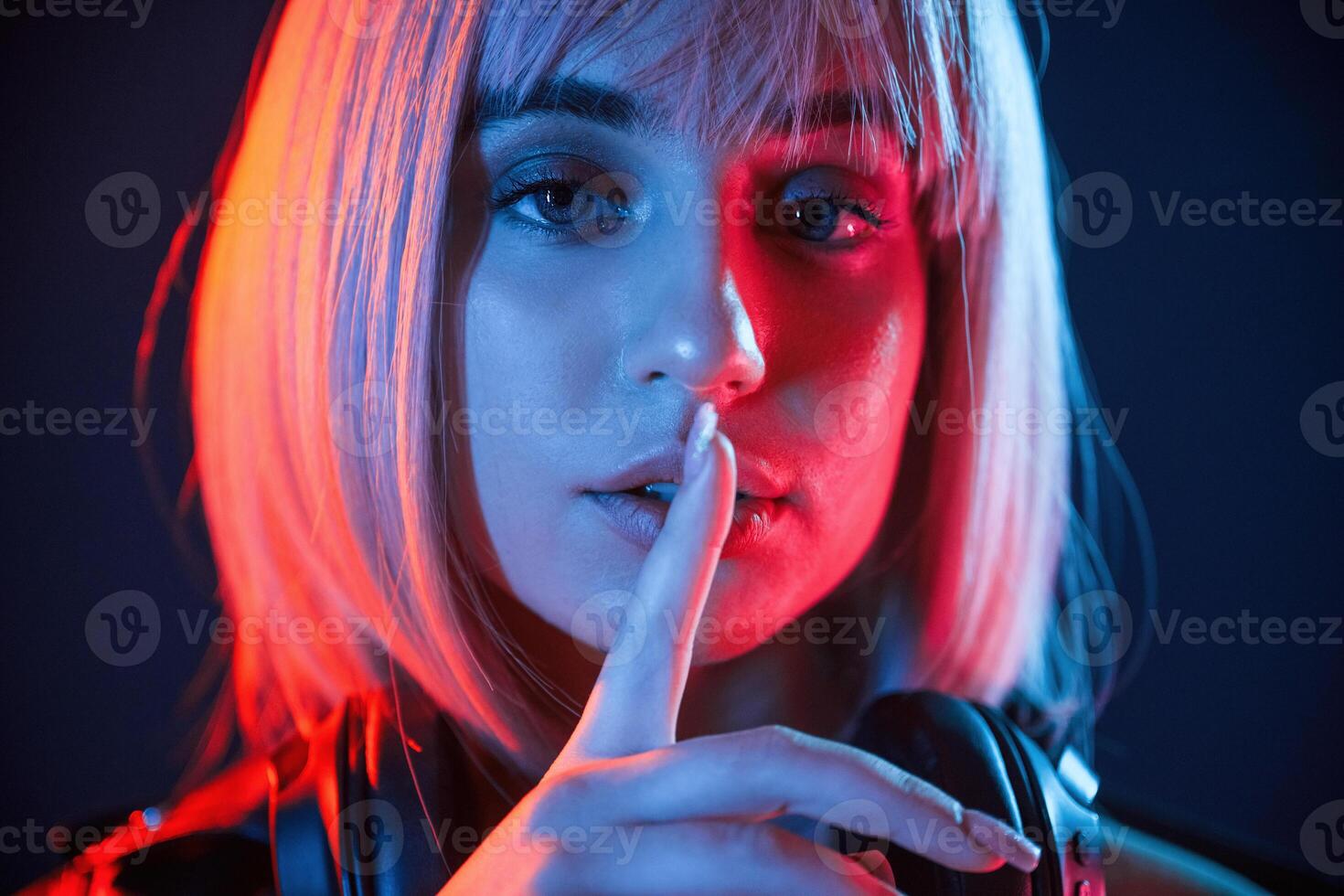 Gesture of be quiet,,, finger is by the lips. Woman with white hair is in studio with neon colors photo