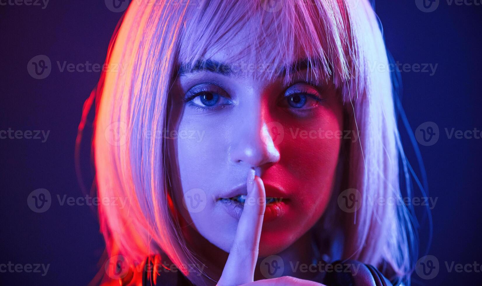 Gesture, of be quiet, finger is by the lips. Woman with white hair is in studio with neon colors photo